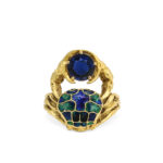 Gold ring in the form of a crab with green and blue enamel shell holding a sapphire with its claws