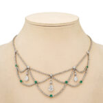 emerald and diamond swag necklace photographed on a beige neck block