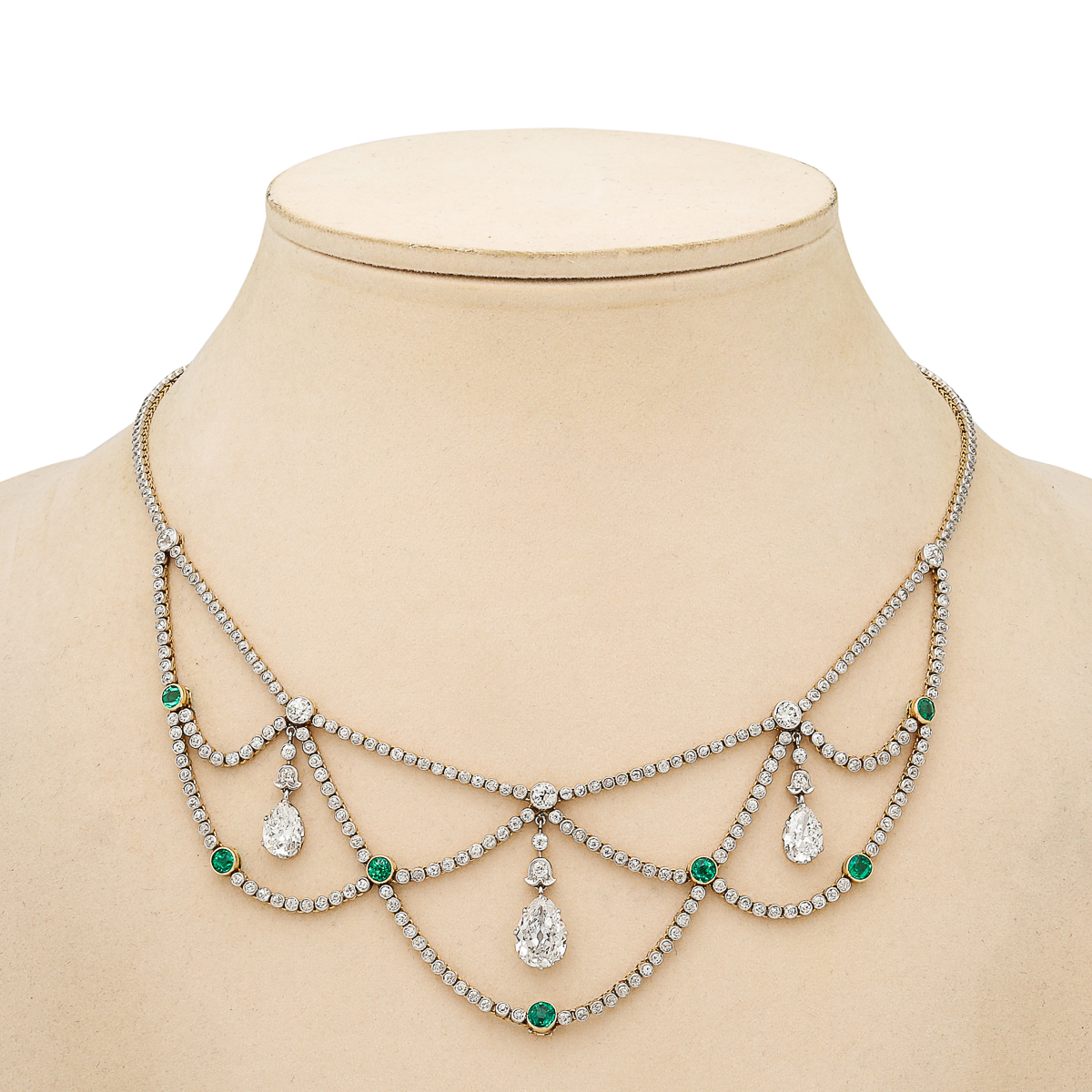 emerald and diamond swag necklace photographed on a beige neck block