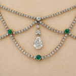 detail view of diamond and emerald swag necklace on beige neck block